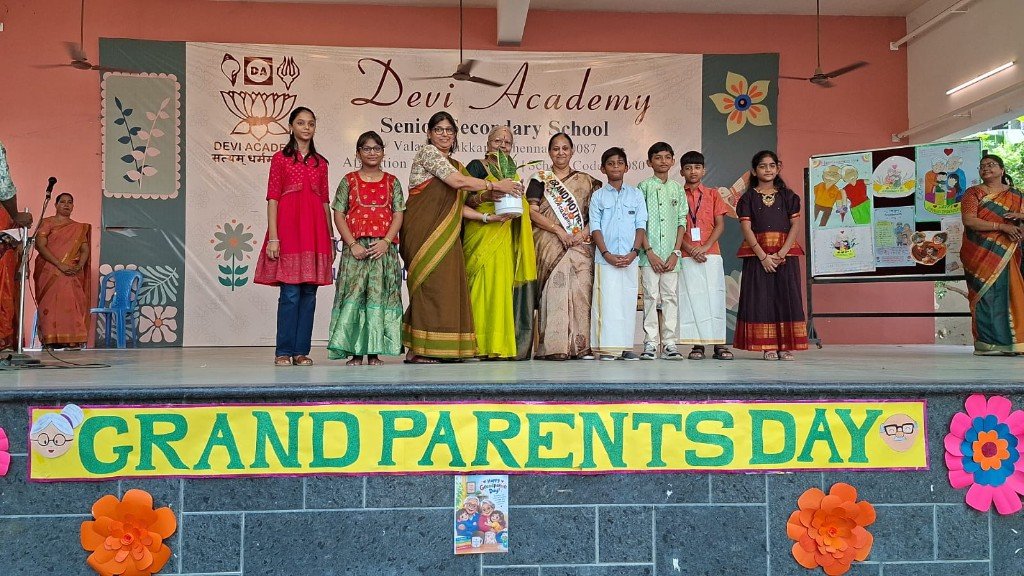 Students and grandparents on stage beneath the Grandparents’ Day banner, as a memento is presented